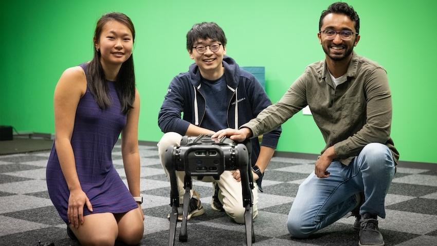 Three students kneel next to a robot dog