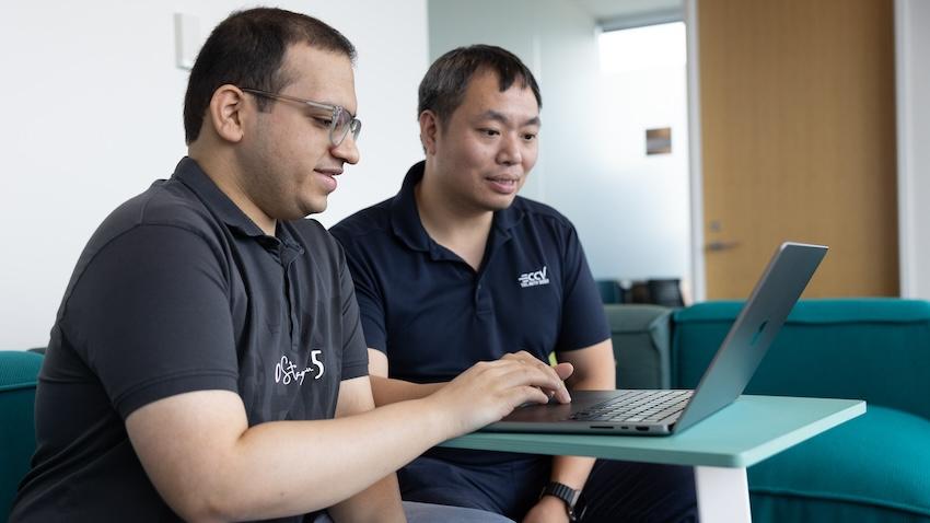 A student and professor sit next to each other looking at a laptop